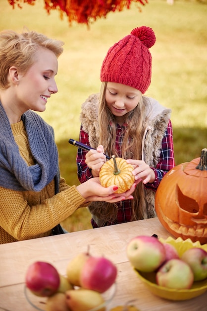 Mother helping daughter in decorating a pumpkin