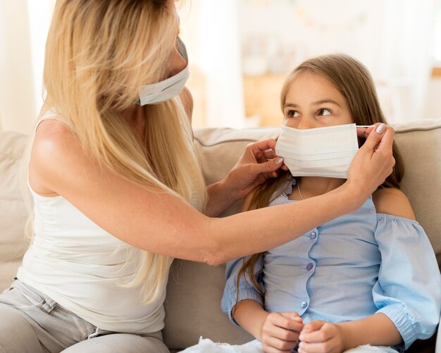 Mother helping daughter to put on medical mask