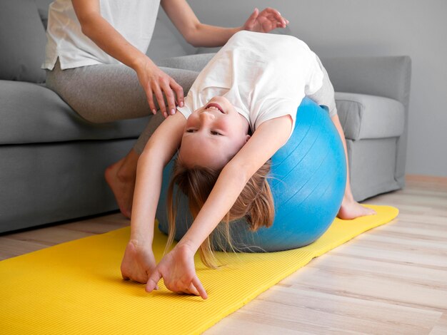 Mother helping girl to exercise on ball