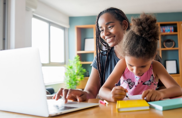 Mother helping and supporting her daughter with online school while staying at home. New normal lifestyle concept. Monoparental concept.