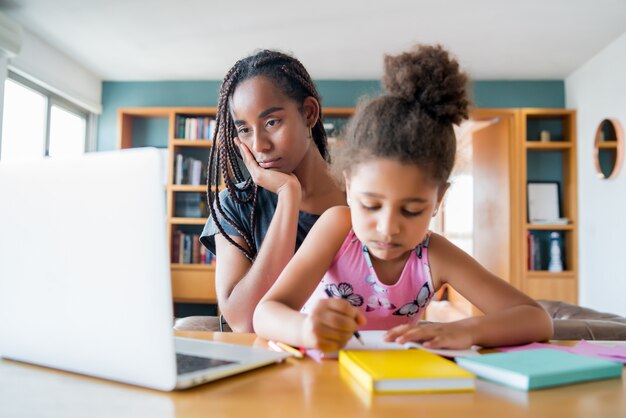 Mother helping and supporting her daughter with online school while staying at home. New normal lifestyle concept. Monoparental concept.