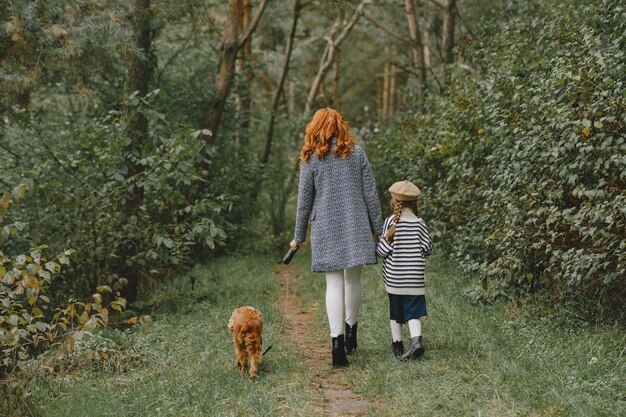 犬と遊ぶ母と娘。秋の公園の家族。ペット、家畜、ライフスタイルのコンセプト。秋の時間。