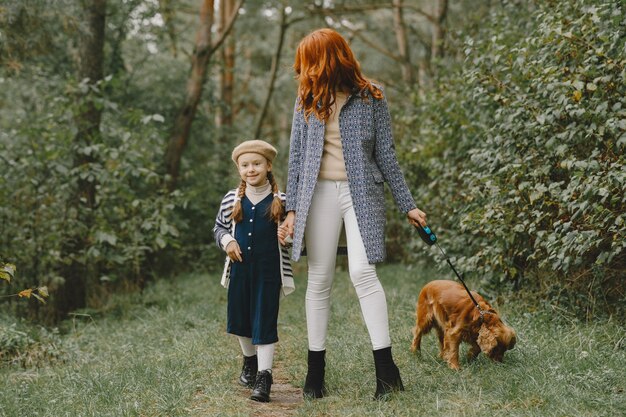 Mother and her daughter playing with dog. Family in autumn park. Pet, domestic animal and lifestyle concept. Autumn time.