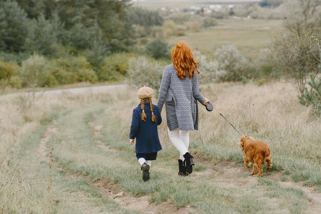 犬と遊ぶ母と娘。秋の公園の家族。ペット、家畜、ライフスタイルのコンセプト。秋の時間。