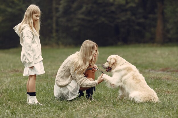 犬と遊ぶ母と娘。秋の公園の家族。ペット、家畜、ライフスタイルのコンセプト