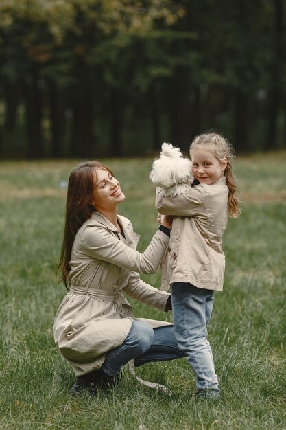 Mother and her daughter playing with dog. Family in autumn park. Pet, domestic animal and lifestyle concept