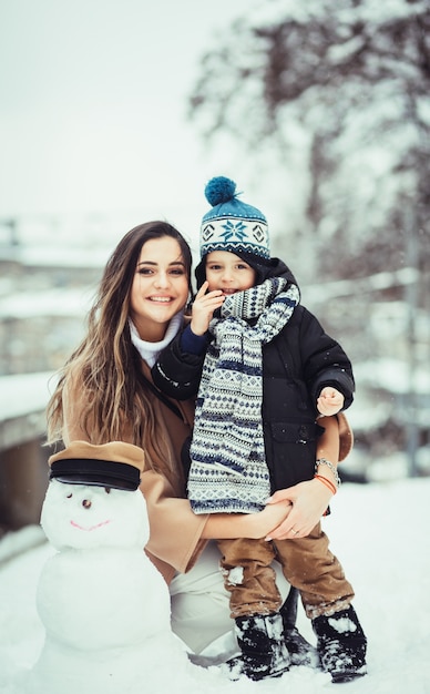 Foto gratuita la madre e suo figlio seduti vicino pupazzo di neve