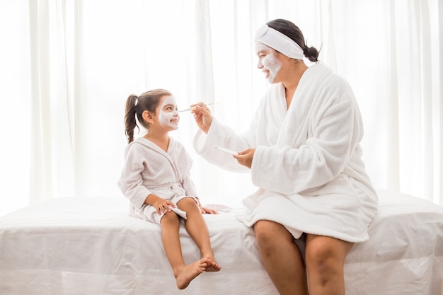 Мать и ее молодая симпатичная дочь развлекаются в спальне и делают глиняные маски для лица