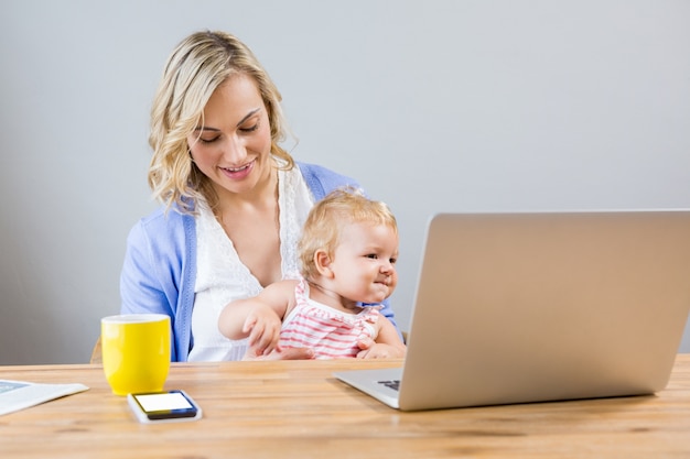 Mother holding baby girl while using laptop