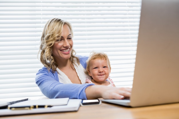 Mother holding baby girl while using laptop