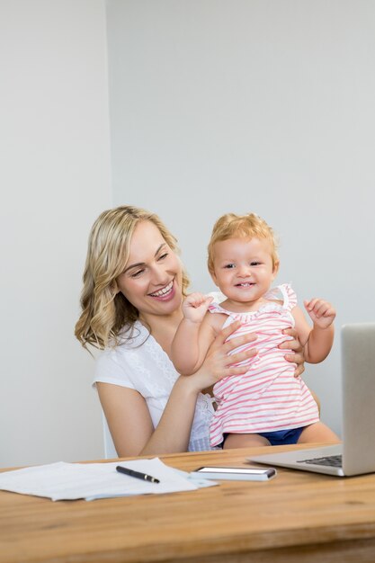 Mother holding baby girl while using laptop