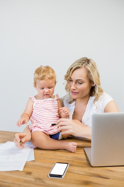 Mother holding baby girl while writing notes on paper