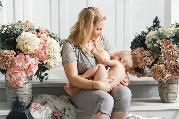 모유 수유 전에 그녀의 무릎에 아기를 들고 어머니. 꽃 장식에서 촬영 스튜디오