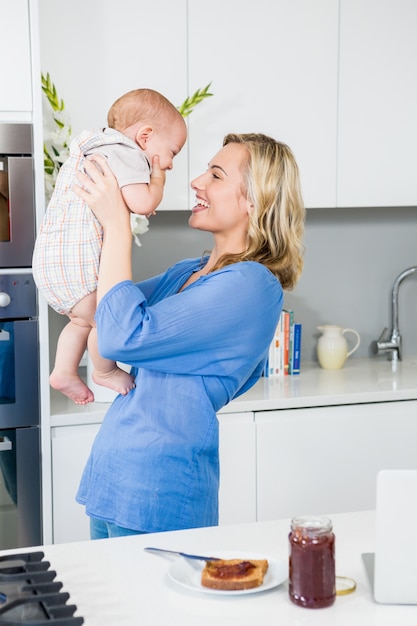 Free photo mother holding her baby boy in kitchen