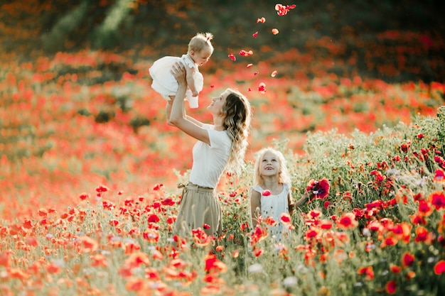 Free photo mother holds her baby at height, her elder daughter smiles on the poppy field