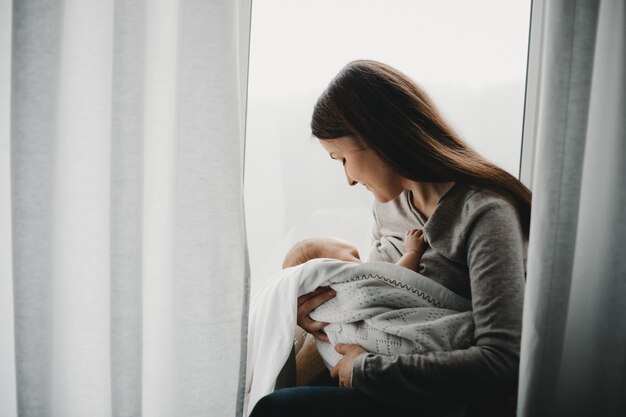 Mother holds newborn boy on her arms while she feeds him