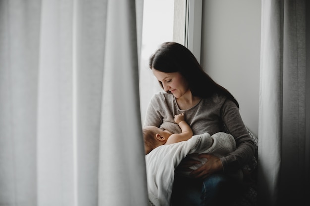 Mother holds newborn boy on her arms while she feeds him