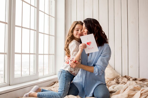 Mother hugging cute daughter with greeting card