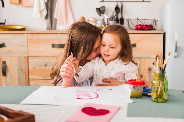 Mother hugging daughter while she painting heart