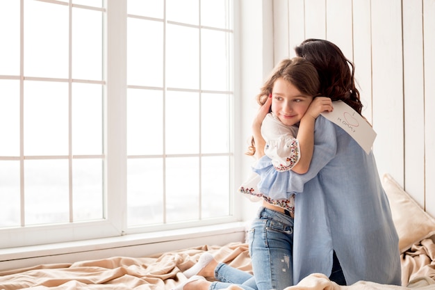 Free photo mother hugging daughter with greeting card