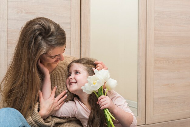 Mother hugging daughter with tulip flowers 