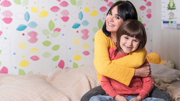 Mother hugging little daughter from behind on bed