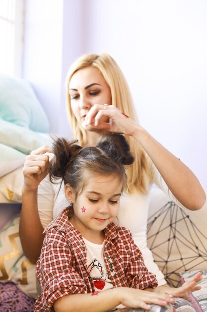 Mother is doing daughter's hair in bright full of sun light room