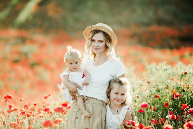 Mother keeps her baby and hugs  her elder daughter on the poppy field