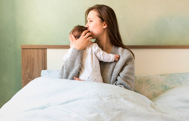 Мать целует ребенка на руках в постели