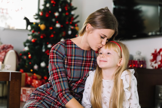 Free photo mother kissing daughter in front of christmas tree