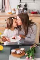 Free photo mother kissing daughter with cupcake