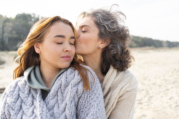 mother kissing her daughter while on the beach
