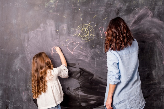 Mother and little daughter drawing on blackboard 