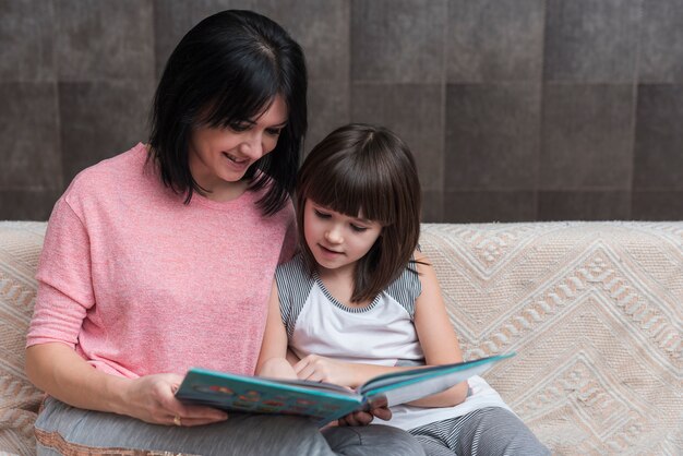 Mother and little daughter reading book on couch