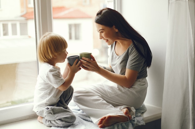 Mother and little son sitting on a windowsill with a tea