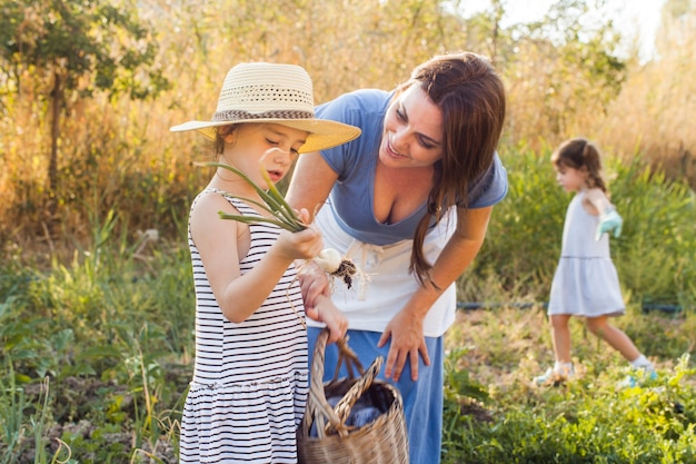 Бесплатное фото Мать смотрит на дочь, собирает лук в поле