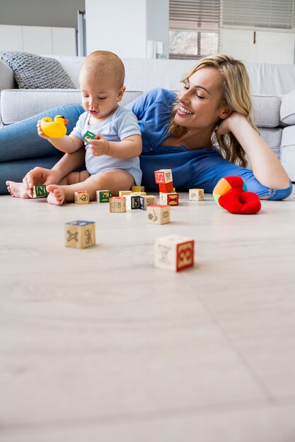 Mother looking at baby boy playing with toys in living room