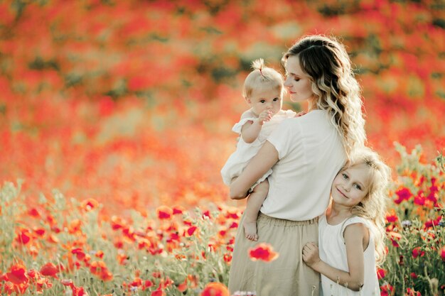 Mother looks at her baby, elder daughter nestles to mom on the poppy field