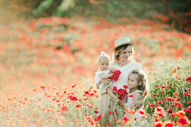 Mother looks at her elder daughter and holds a baby on the poppy field