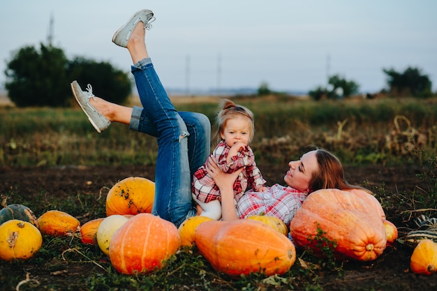 Mother lying on pumpkins with legs up and daughter in her stomach