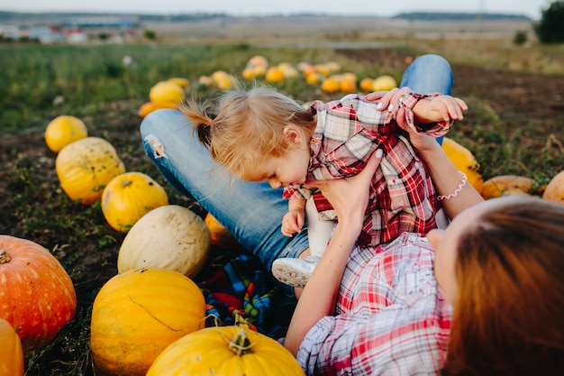 Mother lying on pumpkins with legs up and holding daughter in her stomach