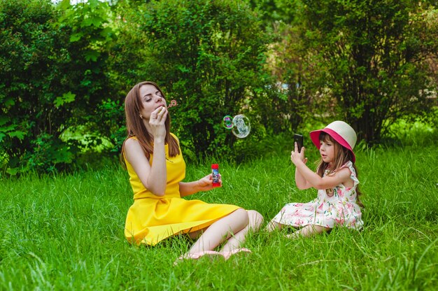 Mother making bubbles while her daughter takes pictures of her