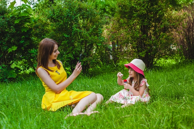 Mother photographing her daughter while blowing soap bubbles