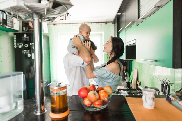 Mother playing with baby sitting on man's shoulder standing in the kitchen