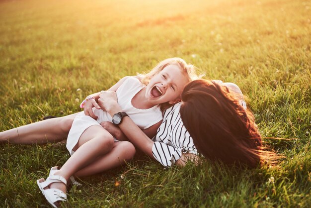 Mother plays with her daughter on the street in the park at sunset