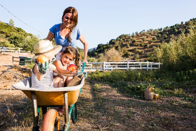 Mother pushing her daughters in wheelbarrow at field