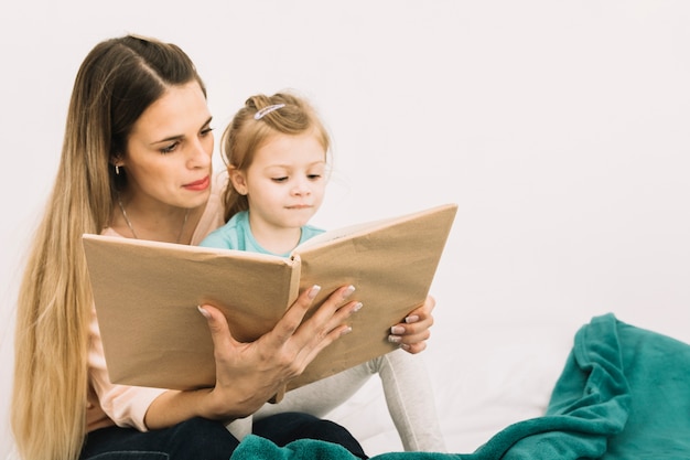 Mother reading book to cute girl on bed