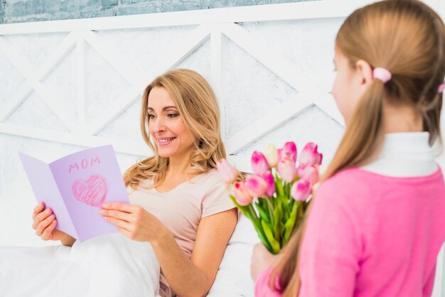 Mother reading greeting card in bed 