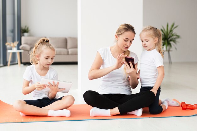 Mother showing something to daughters on smartphone while working out