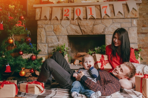 Mother sitting on the floor while the father rests his head on her lap and holds the baby with one arm